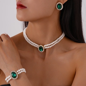 Detail view of double-layered pearl jewelry set with emerald gemstones and gold finish