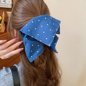 Détail d'un nœud papillon bleu en tissu à motifs cœurs porté par une femme sur les cheveux