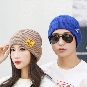 Pair of khaki and blue knit beanies with Moment of Ambitions patches for winter warmth