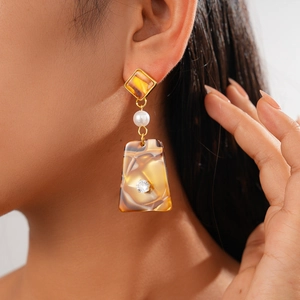 Gros plan de boucles d'oreilles géométriques en résine ambre avec perles sur modèle