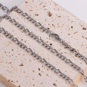 Silver 4.5mm Figaro chain necklace with lobster clasp on beige travertine base