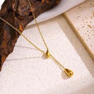 Collier minimaliste à pendentif goutte dorée pour femme sur un support en bois texturé