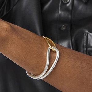 Detail of two-tone gold and silver open cuff bracelet on model in black leather outfit