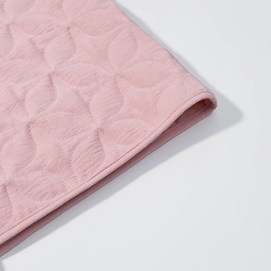 Macro detail of leaf-patterned quilting on pink soft cotton jacket with fine stitching