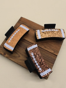 Detail of three glitter football claw clips in gold and bronze on a dark wooden board