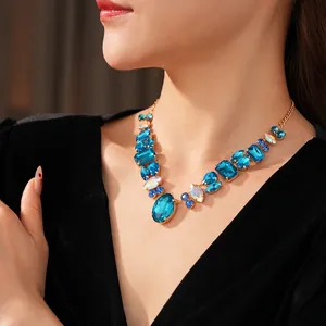 Luxurious V-shaped gold necklace with sparkling blue gemstones worn with black velvet dress