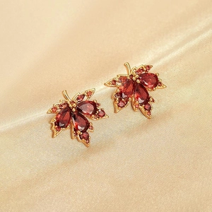 Détail de boucles d'oreilles feuille d'érable avec gemmes rouges sur soie champagne
