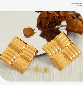 Macro detail of gold square vintage earrings with quilted relief on white fabric