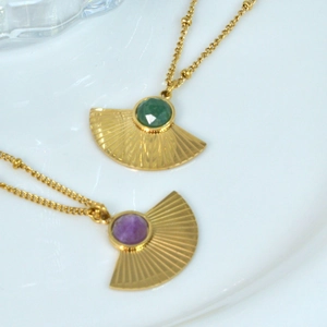 Macro shot of gold fan-shaped pendants with purple and green stones on white plate