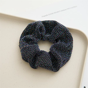 Detailed texture of black pleated scrunchie with colorful glitter threading on a beige tray