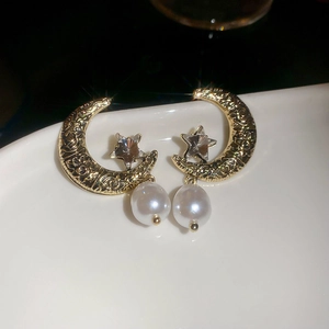 Macro shot of gold star moon earrings with sparkling zircon and white teardrop pearl detail