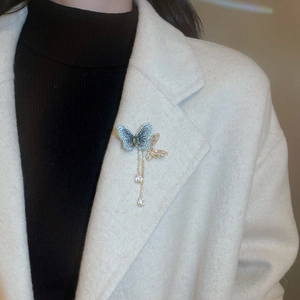 Detail of elegant butterfly brooch with blue beads and long tassels on white wool coat
