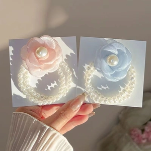 Hand holding elegant camellia flower hair ties with double-layered pearl bands