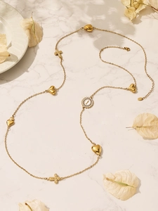 Detail van een lange gouden ketting met hartjes, kruisjes en een ronde munt medaillon