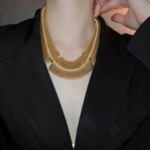 Close-up of chunky gold spiral spring necklace on model in black suit for industrial style