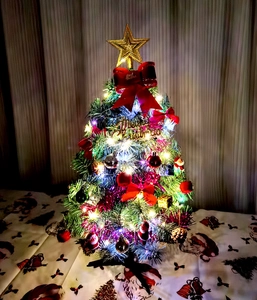 Close-up of a lit mini Christmas tree with red bows, gold balls and LED fairy lights