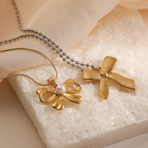 Elegant gold bow pendant necklace set with pearl on polished silk and stone base