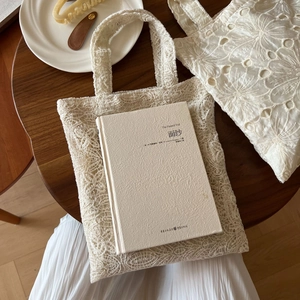 Detail of cream white lace tote bag with floral embroidery on a wooden table