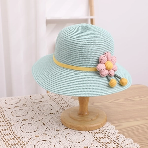 Détail d'un chapeau de soleil en paille vert menthe avec fleur et pompons jaunes