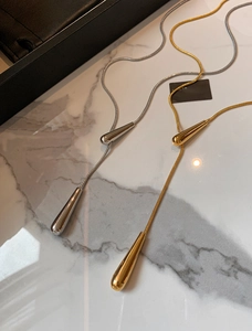 Detail view of gold and silver teardrop pendant necklaces on white marble surface