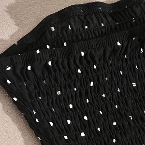 Detailansicht des elastischen Smock-Gewebes mit klassischen weißen Punkten auf schwarzem Kleid