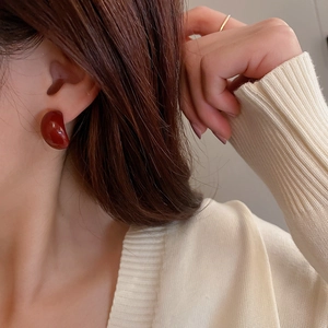 Close-up of elegant deep red glossy heart-shaped stud earrings worn by a model
