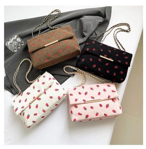 Detail of four colorful corduroy shoulder bags featuring strawberry prints and gold chains