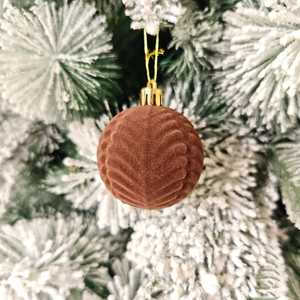 Détail d'une boule de Noël en velours marron avec texture de feuilles sur un sapin