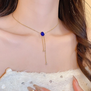 Detail of gold Y-necklace featuring a rectangular blue gemstone and rhinestone tassels