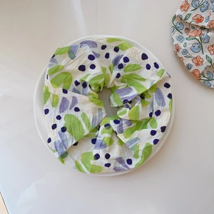 Detailed close-up of a pleated floral scrunchie with green and purple prints on a white plate