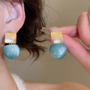 Detail of gold brushed square earrings with teal cat eye stone spheres for women