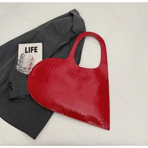 Flat lay of red heart-shaped tote bag in crocodile pattern leather on white fabric background