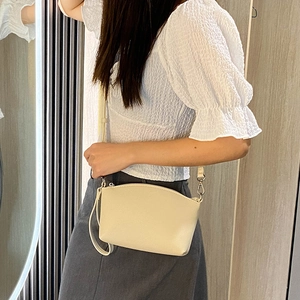 Chic beige leather crossbody bag with silver hardware worn by model against wood wall