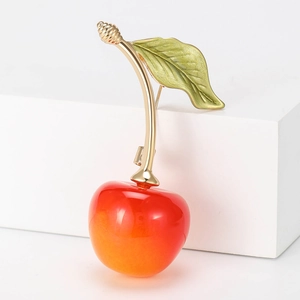 Close-up of elegant cherry brooch with green enamel leaf and red resin fruit