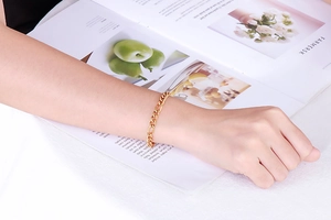 Close-up of a minimalist gold link chain bracelet worn on a model wrist with a magazine