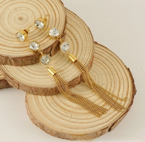 Détail de boucles d'oreilles pampilles dorées avec zircons sur plateau en bois