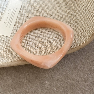 Macro shot of marble textured resin square bangle in peach orange with a glossy finish