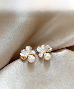 Détail de boucles d'oreilles fleurs et perles sur soie champagne avec bords dorés