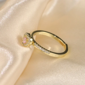 Close-up of pink heart zircon ring with gold band on champagne silk background