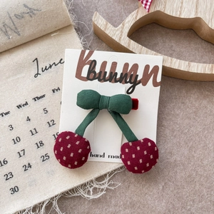 Detail of a handmade cherry-shaped plaid fabric hair clip on a bunny branded card