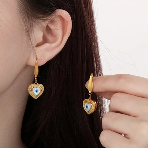 Close-up of heart-shaped evil eye earrings in 18k gold plated titanium on model