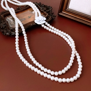 Elegant double-layer long pearl necklace with white camellia pendant on brown leather background