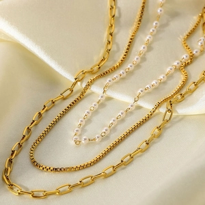 Detail of triple-layered 18K gold-plated chain necklace with small pearls on silk fabric