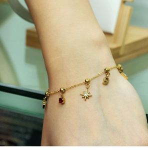 Close-up of gold stainless steel bracelet with ruby, star, and number 9 charms on wrist