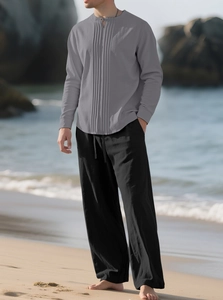 Detail von grauem Faltenhemd und schwarzer Leinenhose vor einem sandigen Strandhintergrund