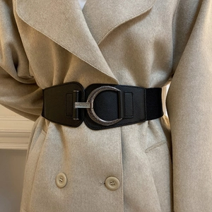 Close-up of a wide black elastic waist belt with a vintage silver round metal buckle on a coat
