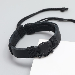 Men's punk leather bracelet with black metal skull and crossbones on white pedestal