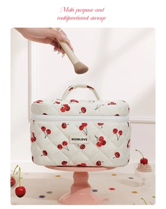 Close-up of white quilted makeup bag with red cherry pattern and sturdy top handle
