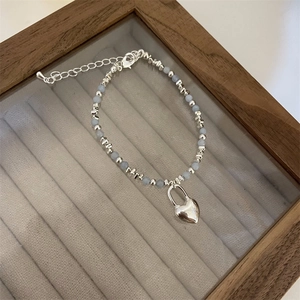 Close-up of light blue frosted beads and silver heart pendant on a stylish beaded bracelet