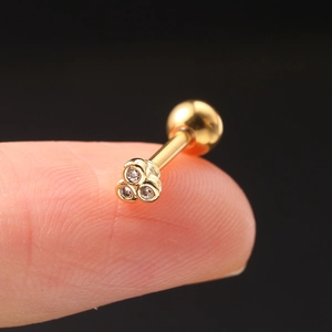 Macro shot of gold-plated triangular stud earring with three zircons on fingertip